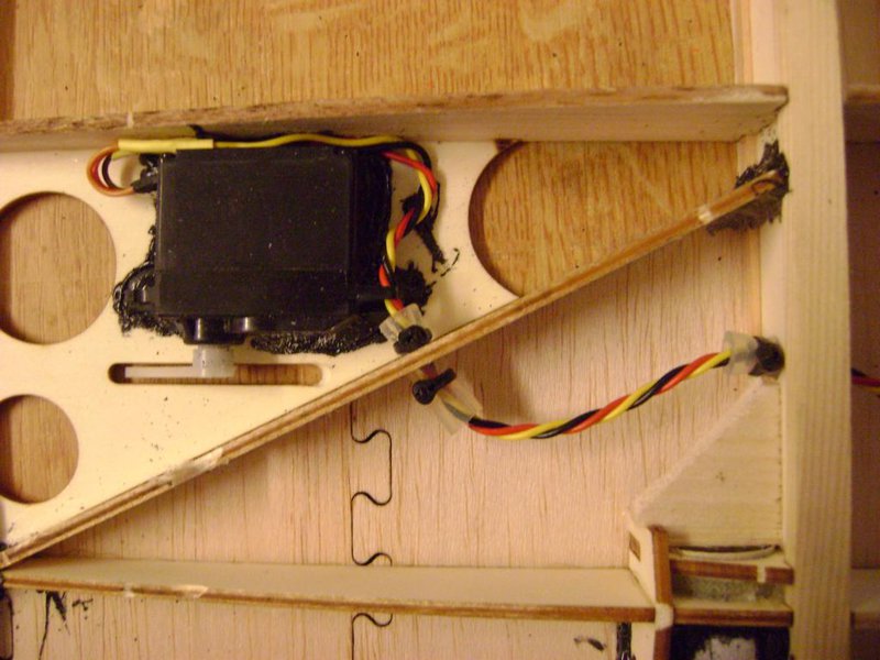 Servoeinbau sollte auch vor der Beplankerei geschehen. Hier zu sehen ist ein viel zu schwerer Standart Servo. Die Kabeldurchführungen hab ich so gross gemacht, das ein stück 8mm Silikonschlauch vor dem scheuern schützt. Mit kleine Kabelbinder werden die Stücke fixiert.